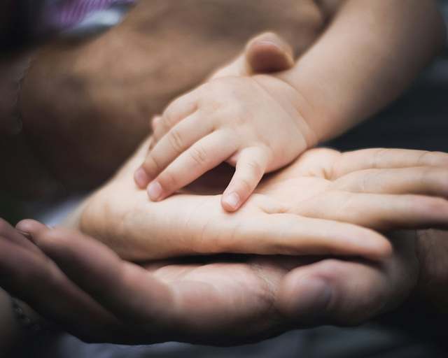 A baby's hand resting on their parents' hands, illustrative photo