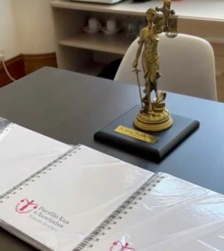 Statue of Themis on the firm's desk, next to folders with the Portillo Kus & Asociados logo
